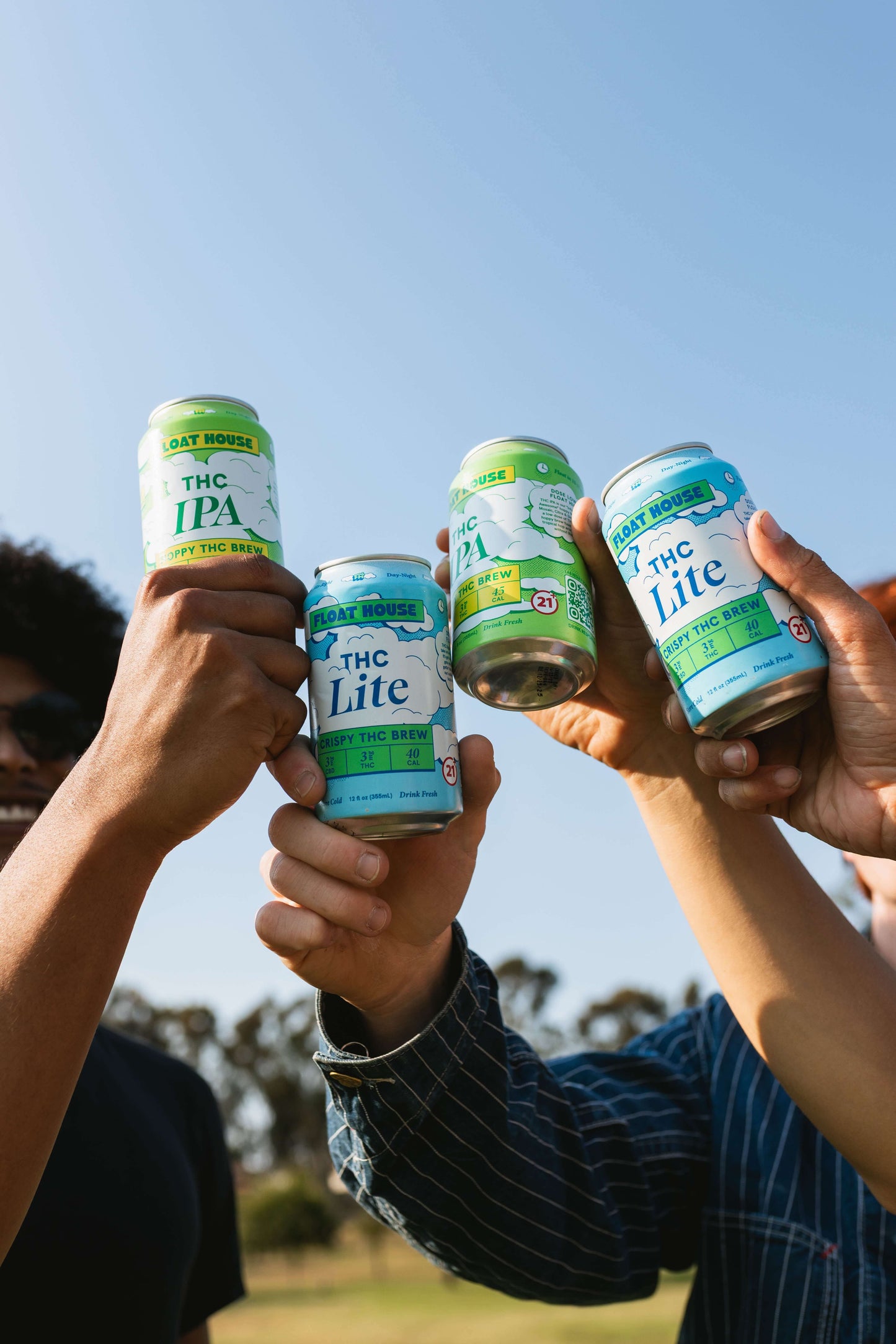 Four cans of 'THC Lite' and 'THC IPA' being held up against a clear blue sky.