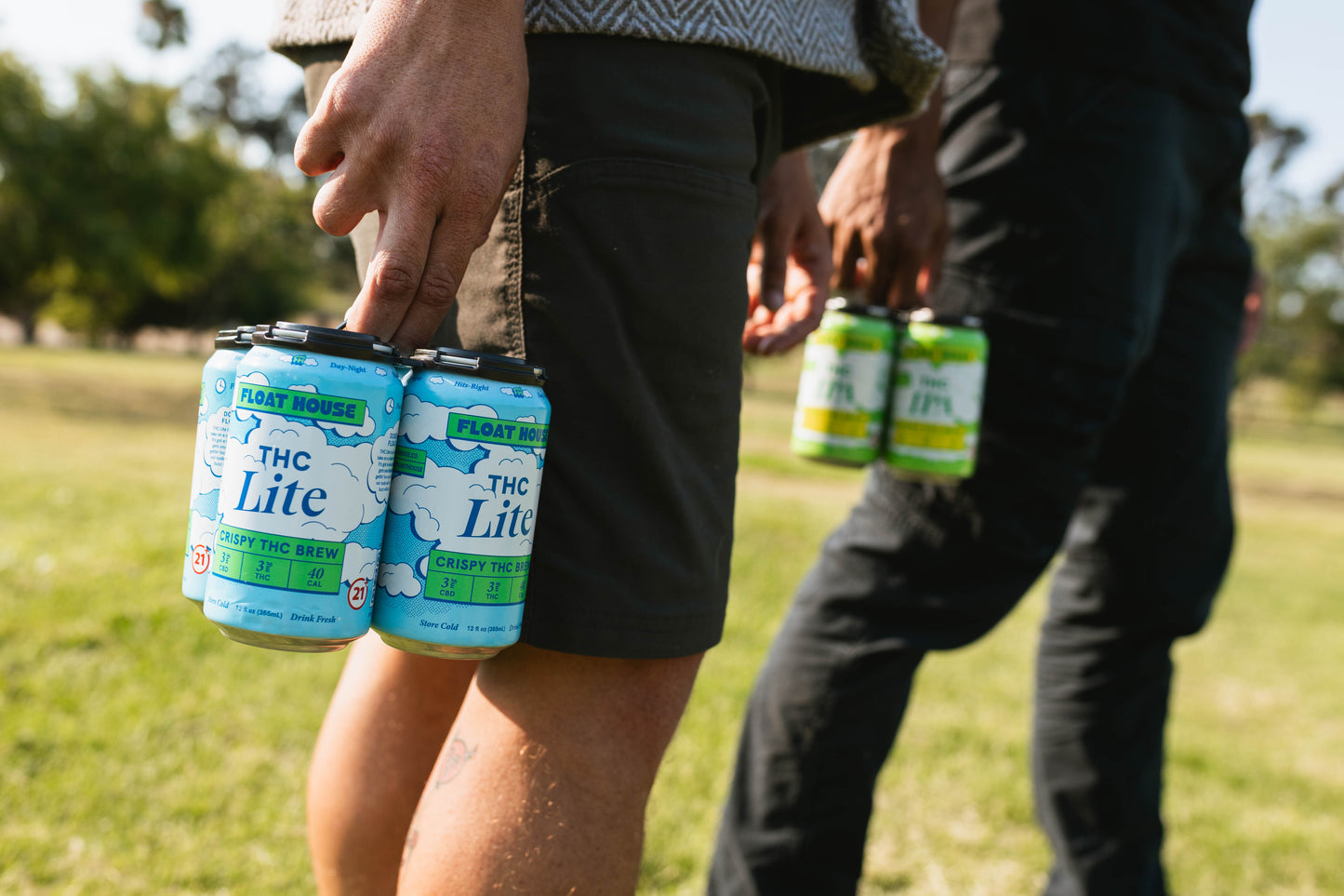 Person holding cans of 'THC Lite' brew in a park setting